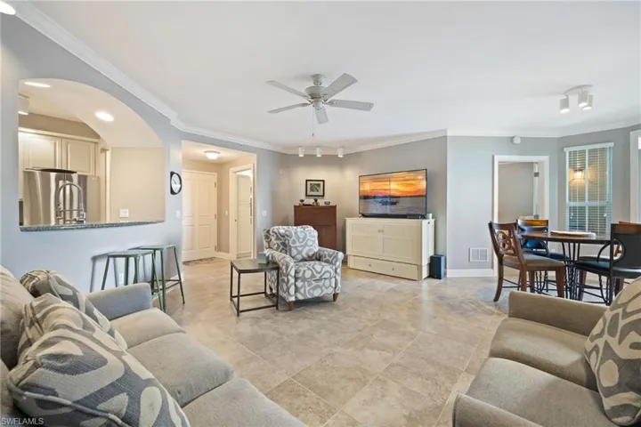 Living area with crown molding, arched walkways, and ceiling fan