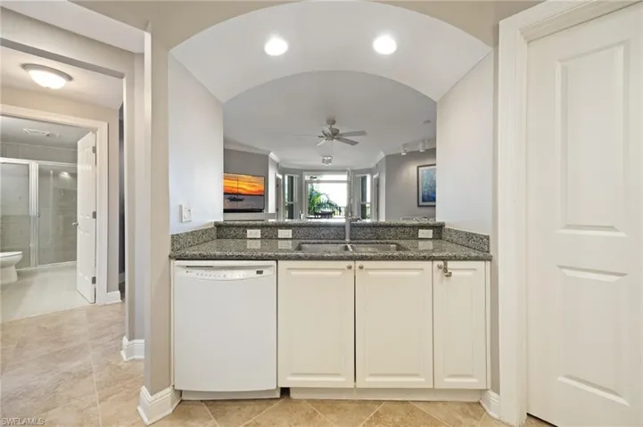 Kitchen featuring dishwasher, ceiling fan, dark stone counters, white cabinetry, and light tile patterned floors