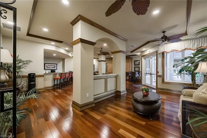 Living room with ornate columns, dark wood-style floors, a ceiling fan, arched walkways, and ornamental molding