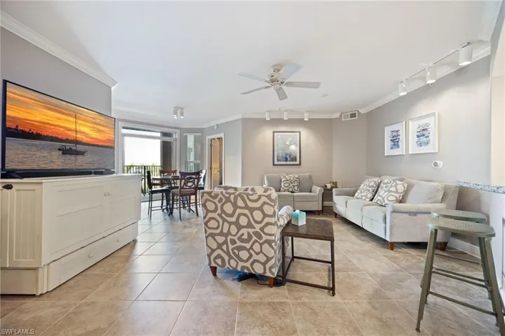 Living room featuring track lighting, crown molding, light tile patterned flooring, and ceiling fan