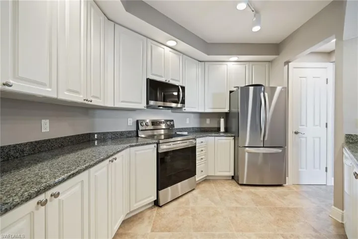 Kitchen with stainless steel appliances, white cabinets, dark stone counters, light tile patterned floors, and rail lighting