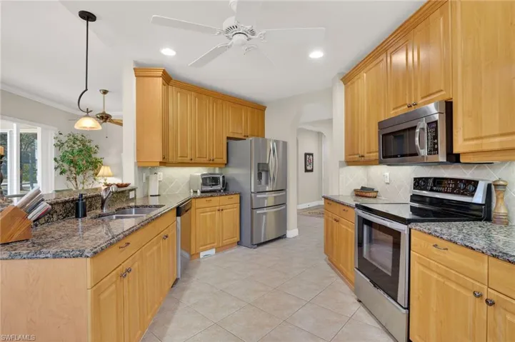 Kitchen with stainless steel appliances, dark granite counters, decorative light fixtures, and light tile patterned flooring