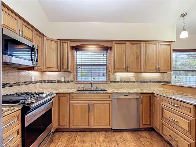 Kitchen with stainless steel appliances, light stone counters, and wood finish cabinetry
