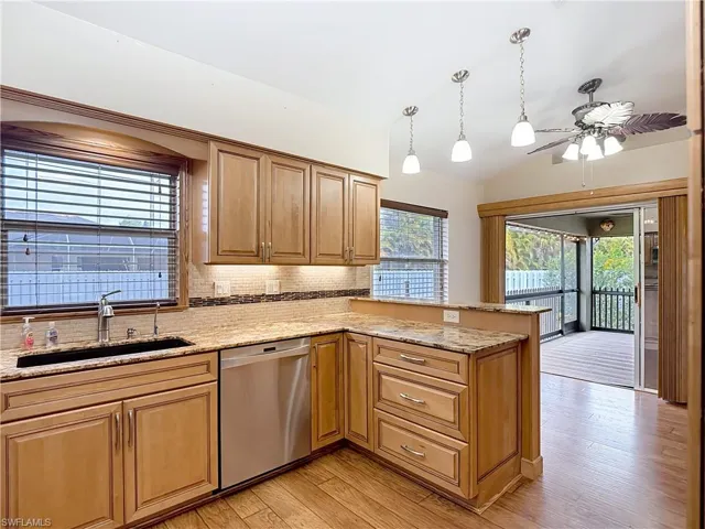 Kitchen featuring hanging light fixtures, light stone counters, dishwasher, lofted ceiling, and ceiling fan