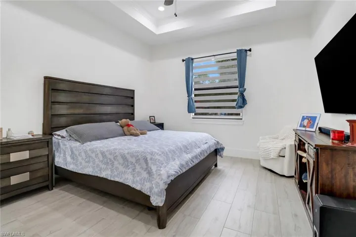 Bedroom with a raised ceiling, ceiling fan, and light wood-type flooring