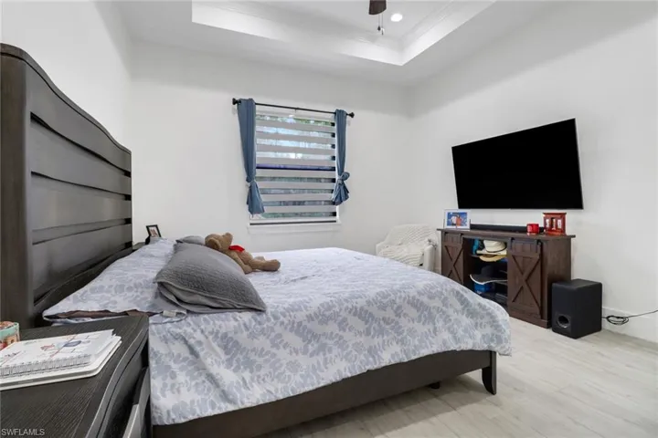 Bedroom with light wood-type flooring, ceiling fan, and a raised ceiling