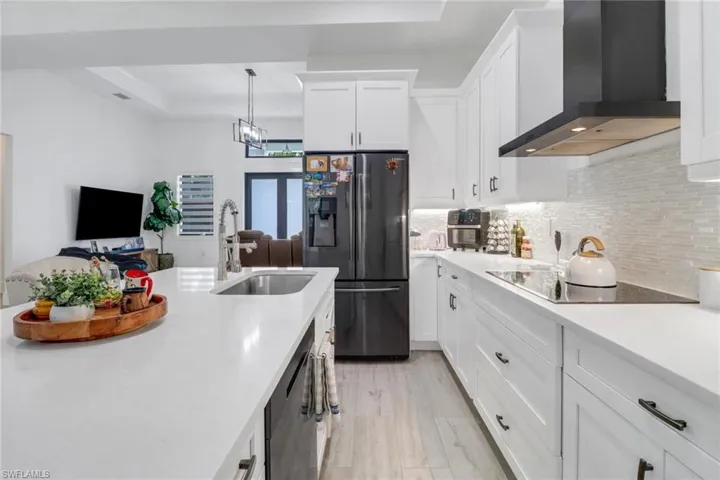 Kitchen with black electric stovetop, wall chimney range hood, white cabinets, decorative backsplash, and stainless steel fridge with ice dispenser