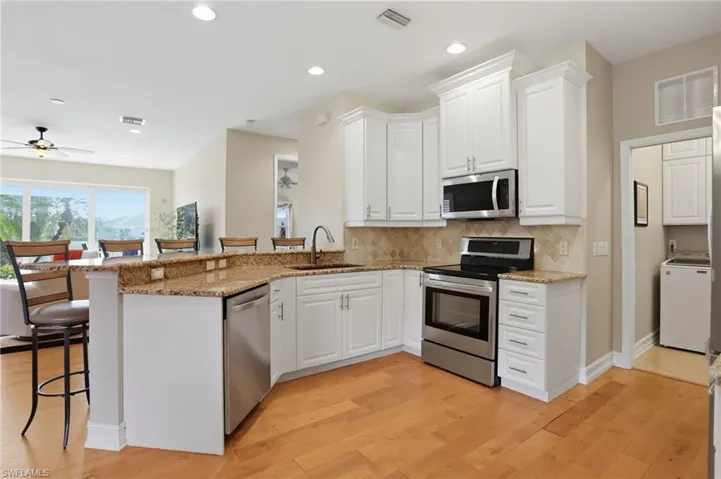 Kitchen with a kitchen breakfast bar, stainless steel appliances, light stone counters, a peninsula, and white cabinets