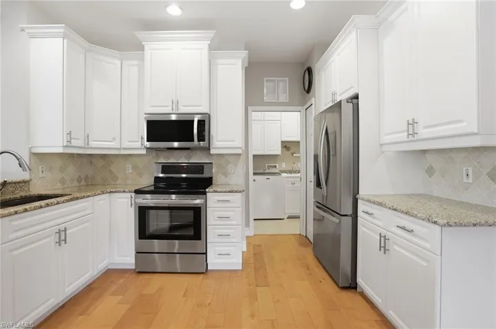Kitchen with stainless steel appliances, light stone countertops, white cabinetry, light wood finished floors, and recessed lighting