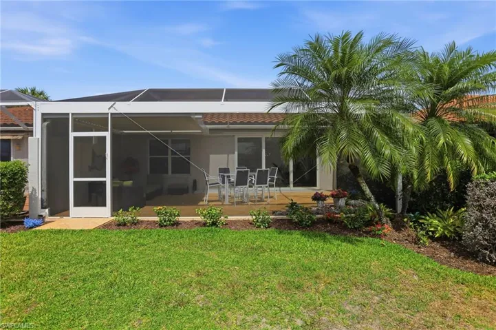Back of house featuring a sunroom, a yard, outdoor dining space, a patio area, and glass enclosure