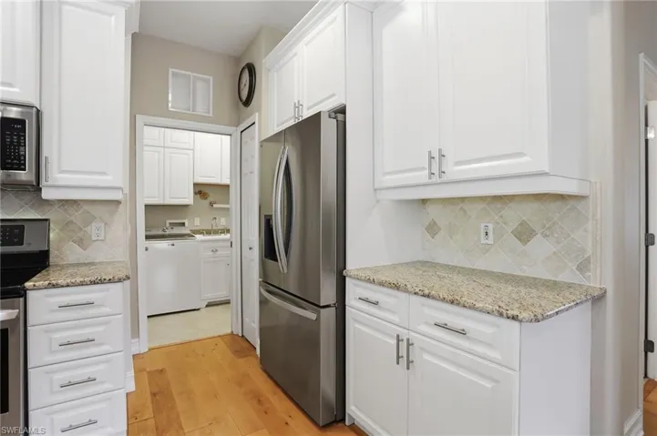 Kitchen featuring stainless steel appliances, white cabinets, decorative backsplash, and light stone counters