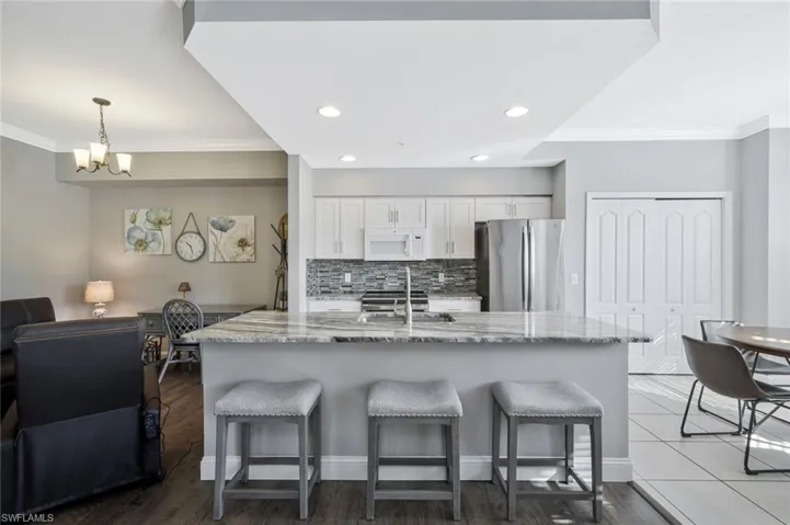 Kitchen featuring ornamental molding, light stone counters, stainless steel appliances, a breakfast bar, and dark wood finished floors