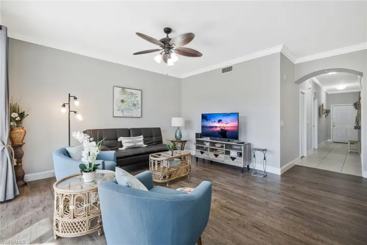 Living area featuring arched walkways, ornamental molding, wood finished floors, and ceiling fan