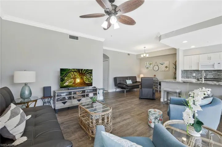 Living area with crown molding, a ceiling fan, arched walkways, dark wood-style floors, and recessed lighting