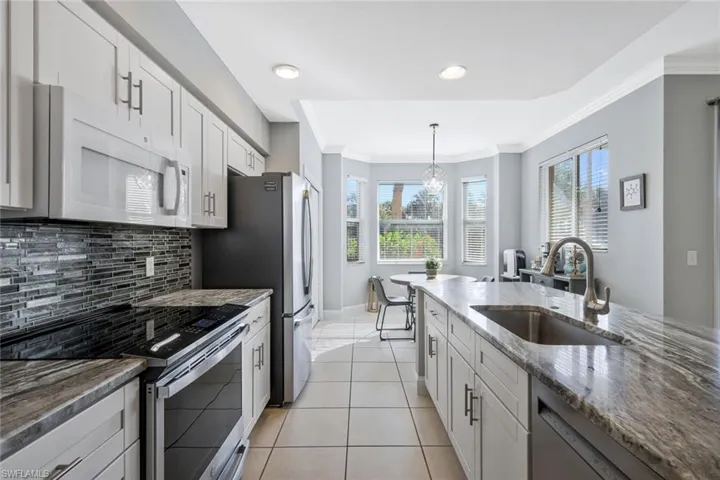 Kitchen with stainless steel appliances, dark stone counters, crown molding, white cabinetry, and light tile patterned floors