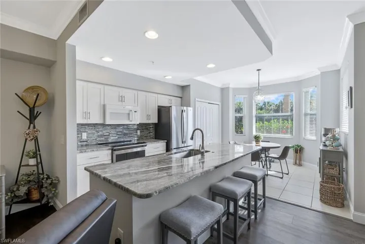Kitchen featuring ornamental molding, light stone countertops, white cabinets, pendant lighting, and stainless steel appliances