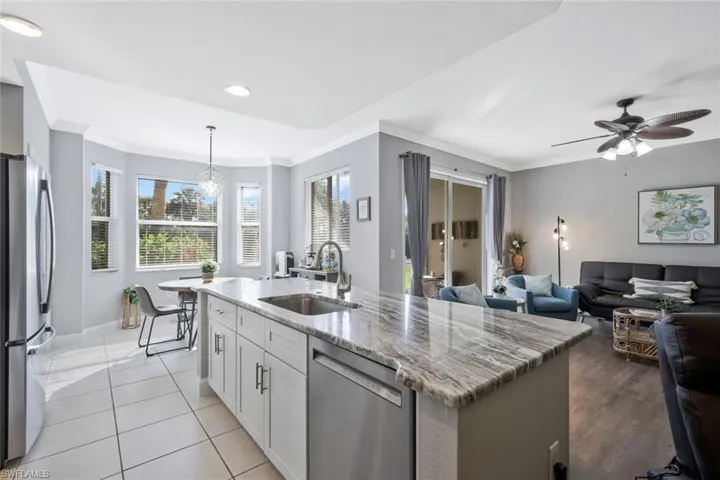 Kitchen featuring light stone counters, stainless steel appliances, open floor plan, an island with sink, and pendant lighting