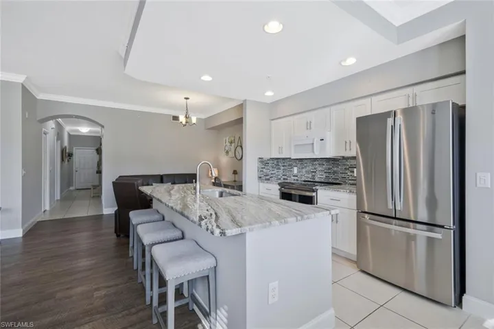 Kitchen featuring stainless steel appliances, ornamental molding, light stone counters, white cabinetry, and a breakfast bar area