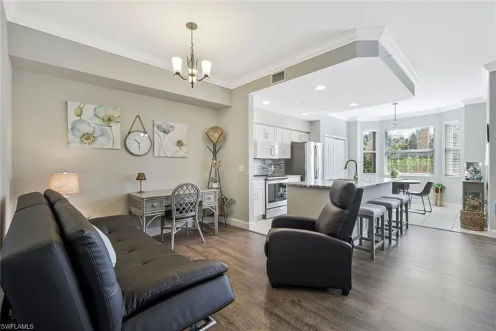 Living room featuring hanging lights, crown molding, and dark wood-style flooring