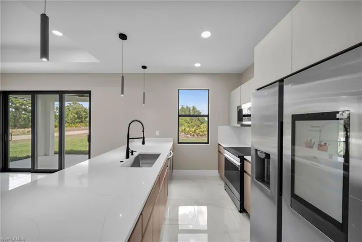 Kitchen with stainless steel appliances, hanging light fixtures, modern cabinets, light stone counters, and white cabinetry
