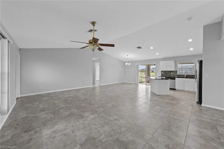 Unfurnished living room featuring vaulted ceiling, ceiling fan, baseboards, recessed lighting, and a chandelier