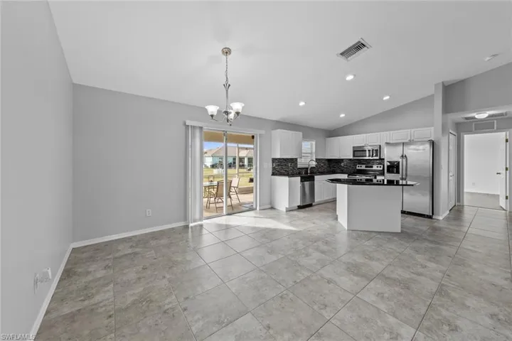 Kitchen featuring stainless steel appliances, a chandelier, lofted ceiling, tasteful backsplash, and white cabinets