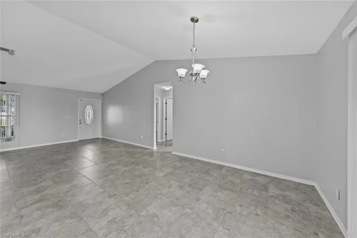 Empty room featuring a chandelier, vaulted ceiling, and baseboards