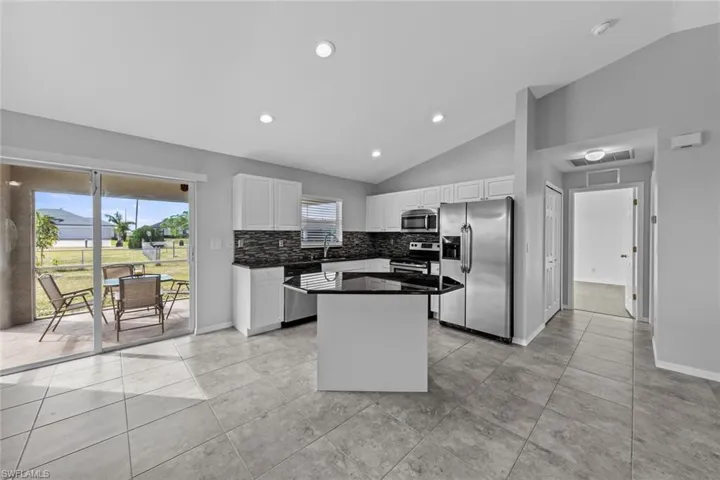 Kitchen featuring appliances with stainless steel finishes, lofted ceiling, a sink, decorative backsplash, and white cabinets