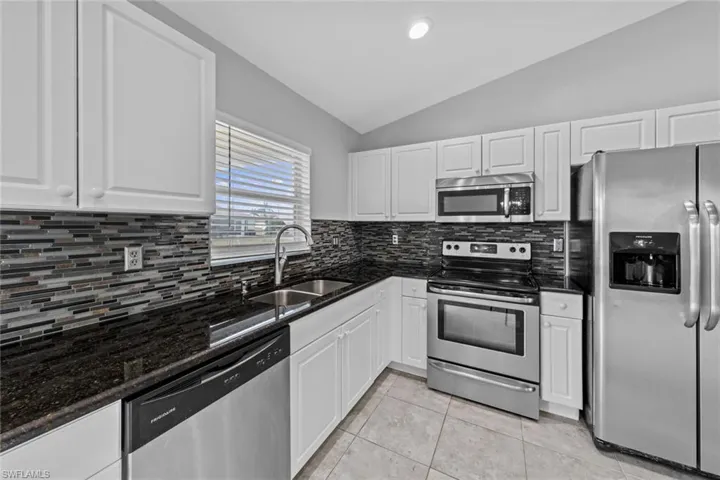 Kitchen with stainless steel appliances, a sink, lofted ceiling, light tile patterned flooring, and white cabinets