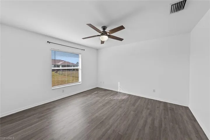 Empty room featuring a ceiling fan, dark wood finished floors, and baseboards
