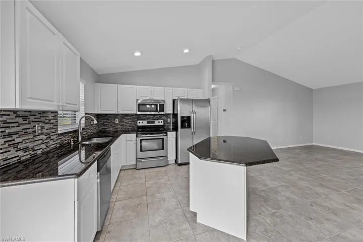 Kitchen featuring appliances with stainless steel finishes, a sink, vaulted ceiling, decorative backsplash, and a kitchen island