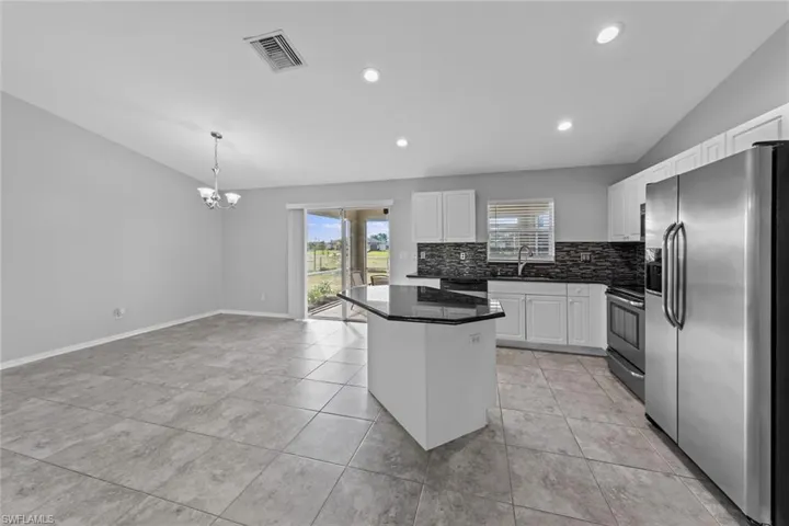 Kitchen with appliances with stainless steel finishes, a sink, backsplash, dark countertops, and a kitchen island
