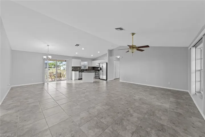 Unfurnished living room featuring a chandelier, lofted ceiling, a ceiling fan, baseboards, and recessed lighting