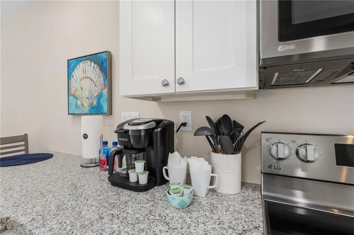 Room details with stainless steel microwave, white cabinets, stove, and light stone countertops