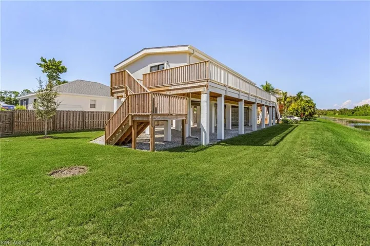 Back of house with stairway, a lawn, a deck, and fence