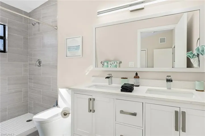 Full bathroom with double vanity, visible vents, a stall shower, and a sink