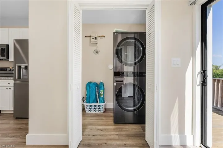 Clothes washing area with stacked washer / dryer, plenty of natural light, and light wood-style flooring