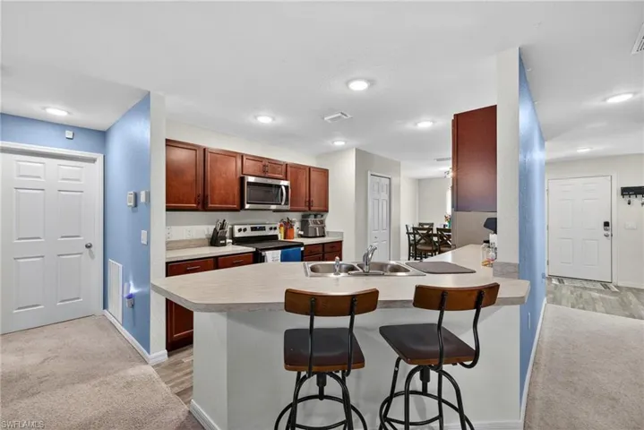 Kitchen with a kitchen breakfast bar, light carpet, stainless steel appliances, light countertops, and a peninsula