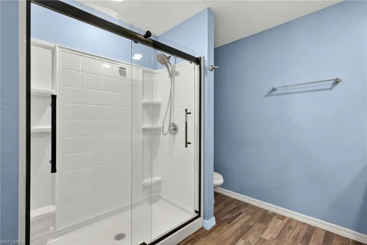 Full bathroom with dark wood finished floors, a stall shower, and a textured wall