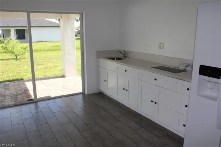 Kitchen with freestanding refrigerator, white cabinetry, dark wood-style flooring, light countertops, and black electric stovetop