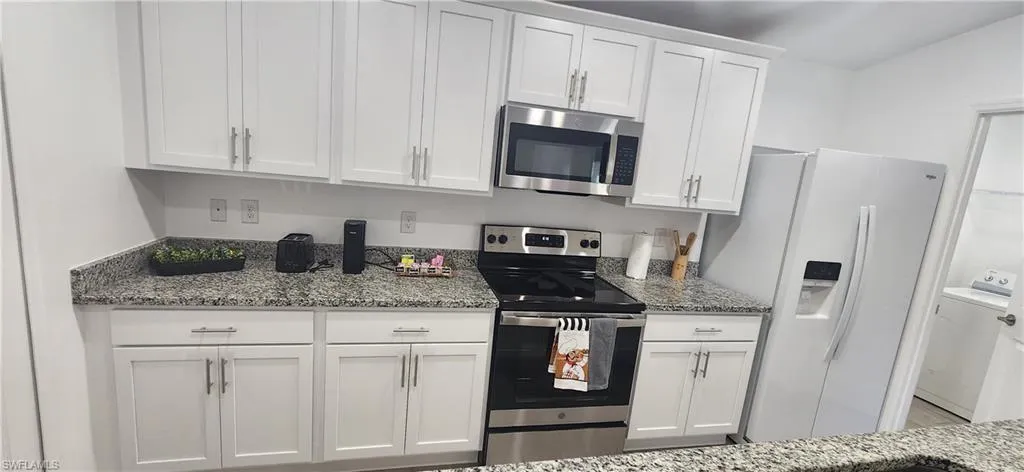 Kitchen with appliances with stainless steel finishes, light stone counters, and white cabinetry