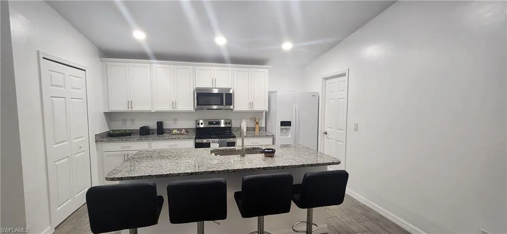Kitchen with stainless steel appliances, white cabinets, light stone countertops, a kitchen breakfast bar, and recessed lighting