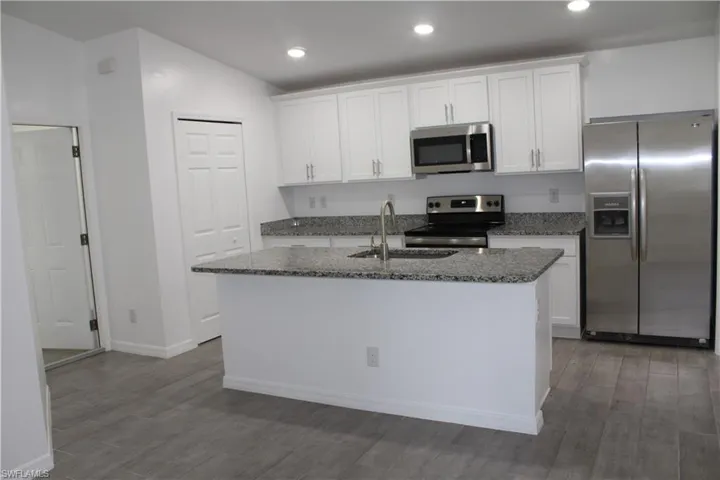 Kitchen with appliances with stainless steel finishes, white cabinetry, a center island with sink, dark wood-style flooring, and dark stone countertops