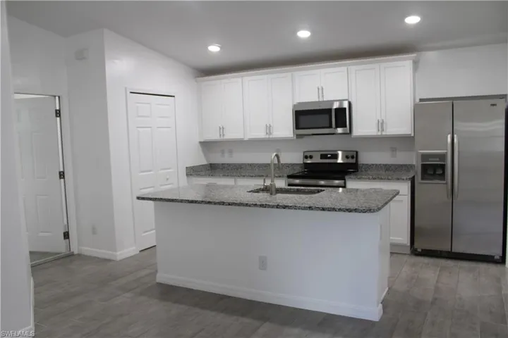 Kitchen featuring appliances with stainless steel finishes, white cabinets, a kitchen island with sink, stone counters, and recessed lighting