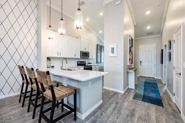 Kitchen featuring range with electric stovetop, a breakfast bar, lofted ceiling, hanging light fixtures, and kitchen peninsula