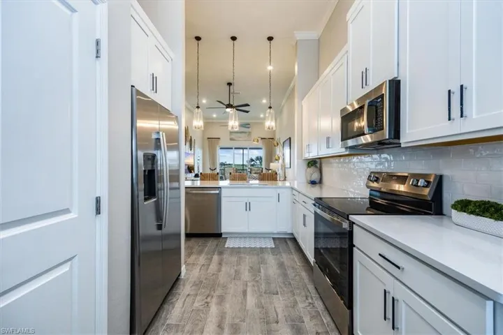 Kitchen with pendant lighting, backsplash, stainless steel appliances, white cabinets, and kitchen peninsula
