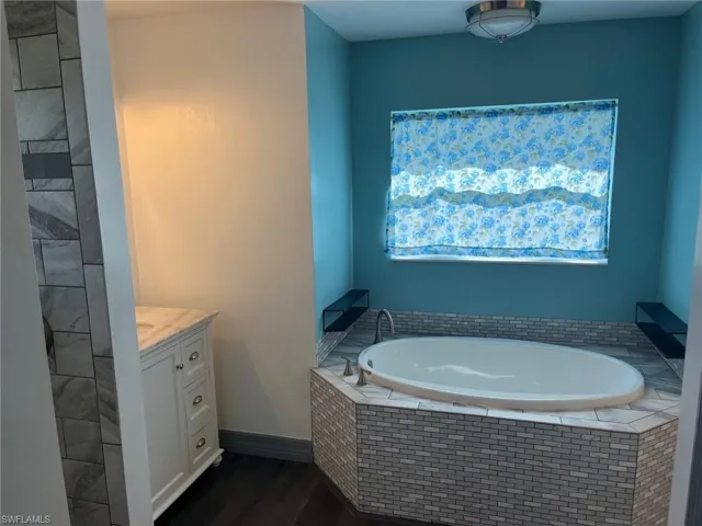 Bathroom featuring a relaxing tiled tub, wood-type flooring, and vanity