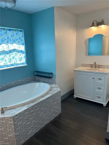 Bathroom featuring vanity, tiled bath, and hardwood / wood-style flooring