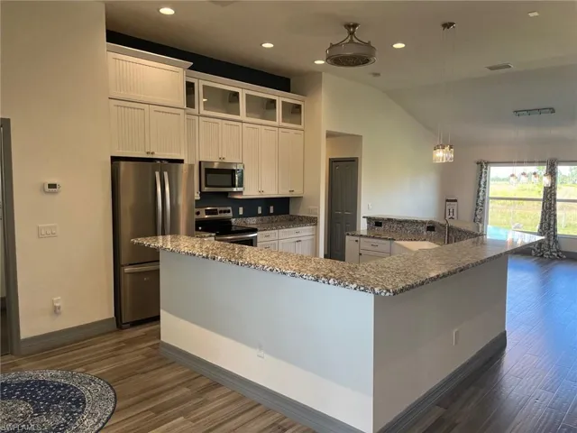 Kitchen featuring stainless steel appliances, a kitchen island with sink, lofted ceiling, white cabinets, and dark hardwood / wood-style flooring