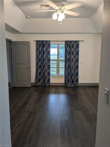 Empty room featuring dark hardwood / wood-style flooring, ceiling fan, and a raised ceiling